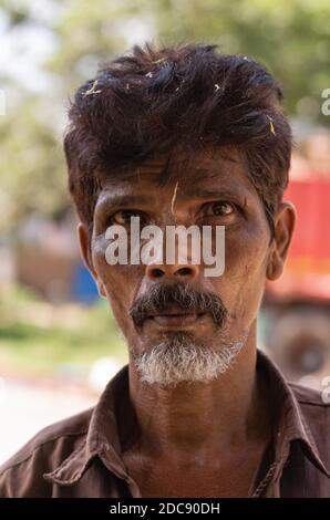 Chikkanayakanahalli, Karnataka, Indien - 3. November 2013: Nahaufnahme Porträt eines ernsthaften bärtigen Mannes mit Stroh in seinem schwarzen Haar. Stockfoto