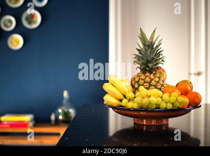 Frisches Obst Schüssel in modernen Innenraum in der Nähe dunkelblaue Wand in der Küche, schöne moderne Design zu Hause. Ananas Bananen und verschiedene Obst retro Haus Stockfoto