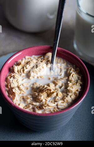 Trocken gerollte Haferflocken in einer Schüssel mit Milch auf dunkelblauem Hintergrund. Stockfoto