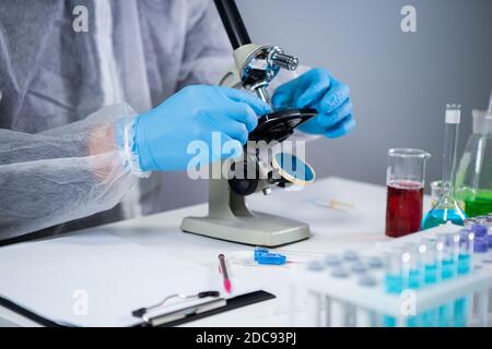 Medizinische Fachkraft in weißen Schutzanzug Blick durch Mikroskop im chemischen Labor. Suche Impfstoff Coronavirus. Covid 19 Arzneimittelerfindungen. Stockfoto