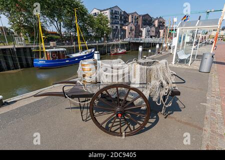 Alte hölzerne Angelwagen mit Krabbenkörben und Rebe Fass Bedeckt mit einem Netz auf dem Marktplatz in Büsum An der Nordseeküste Stockfoto