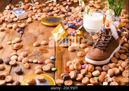 Viele Süßigkeiten auf Holzhintergrund mit Kinderschuh mit Karotten für Santa's Pferd, Pepernoten und Süßigkeiten. Traditionelle niederländische Urlaubspostkarte Sinterklaas . Blick von oben. Speicherplatz kopieren. Stockfoto