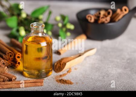 Ätherisches Zimtöl in einer kleinen Flasche, gemahlener Zimt und Zimtstangen auf Steingrund. Stockfoto