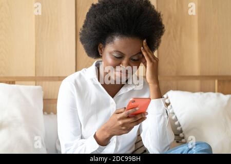 Leben Probleme, brechen mit Freund, schlechte Nachrichten, Herzschmerz. Besorgt afro-amerikanische Frau sitzt auf der Couch hält Handy lesen Nachricht unangenehm Stockfoto