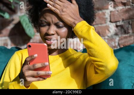 Verwirrt Afro-amerikanische Millennial Frau tun Facepalm Geste, berühren Kopf mit Handfläche, Blick auf Bildschirm Handy, schickte E-Mail an die falsche Addre Stockfoto