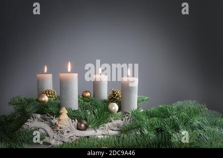 Vier Kerzen brennen zum vierten Advent auf Tannenzweigen mit weihnachtlicher Dekoration vor grauem Hintergrund, Kopierraum, ausgewählter Fokus, schmal Stockfoto