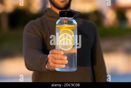 Mann, der eine Flasche frisches Zitronenwasser gibt. Gesunde Getränke, Ernährung und Entgiftung Konzept Stockfoto