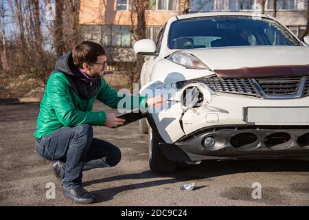 Insurance Agent prüft und den Schaden am Auto zu untersuchen nach einem Unfall. Inspektion des Autos nach einem Unfall auf der Straße. Die vordere fende Stockfoto