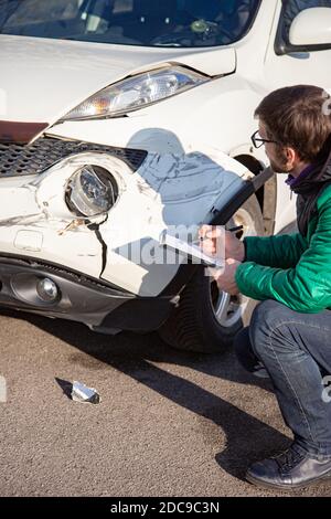 Insurance Agent prüft und den Schaden am Auto zu untersuchen nach einem Unfall. Inspektion des Autos nach einem Unfall auf der Straße. Die vordere fende Stockfoto