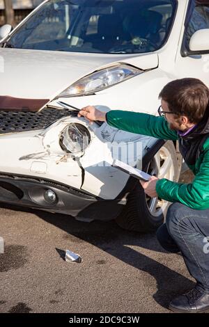 Insurance Agent prüft und den Schaden am Auto zu untersuchen nach einem Unfall. Inspektion des Autos nach einem Unfall auf der Straße. Die vordere fende Stockfoto