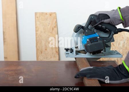 Zimmermann schneidet Holzlatten elektrische Hand Werkzeug Kreissäge auf Schreibtisch, auf Hintergrund orientierte Strangplatte Stockfoto