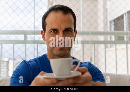 Der 43-jährige Mann in einem blauen Hemd hat eine Tasse Kaffee. Stockfoto