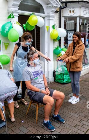 Männer, die ihre Haare abschütteln, um Geld für die Macmillan Cancer Care Charity, High Street, Lewes, East Sussex, Großbritannien zu sammeln. Stockfoto