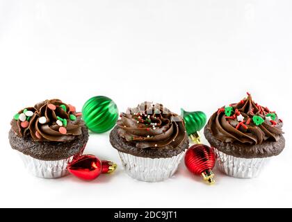 Dreireihige Schokoladen-Weihnachts-Cupcakes mit roten und grünen Ornamenten. Kopieren Sie den Abstand oben auf einen weißen Hintergrund. Stockfoto