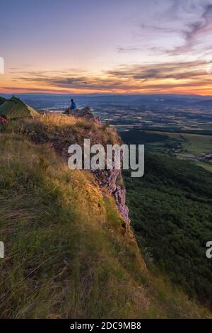 Mann, der auf einer Klippe sitzt und die atemberaubende Landschaft überblickt Bei Sonnenuntergang Stockfoto