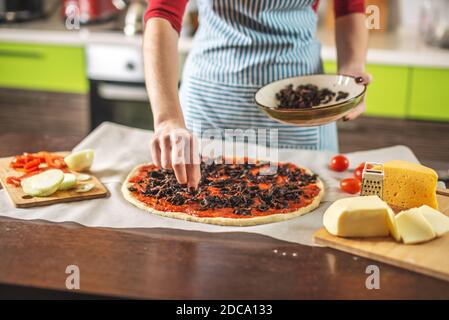 Eine Köchin in einer Schürze setzt Pilze auf eine Pizza roh. Kochen leckere Pizza zu Hause in der Küche. Stockfoto