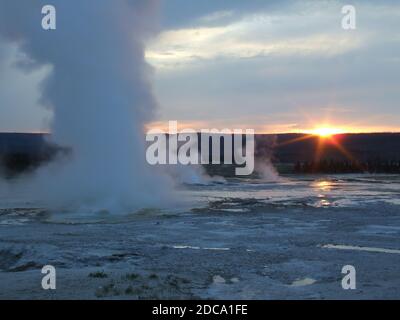 Sonnenuntergang hinter einer Dampfwolke vom Clepsydra Geyser im Lower Geyser Basin des Yellowstone National Park in Wyoming, USA. Stockfoto