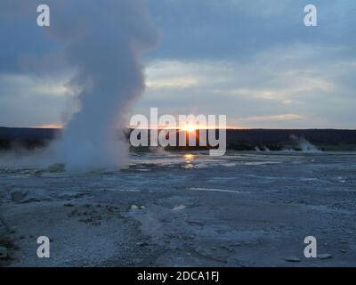 Sonnenuntergang hinter einer Dampfwolke vom Clepsydra Geyser im Lower Geyser Basin des Yellowstone National Park in Wyoming, USA. Stockfoto