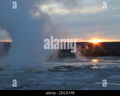 Sonnenuntergang hinter einer Dampfwolke vom Clepsydra Geyser im Lower Geyser Basin des Yellowstone National Park in Wyoming, USA. Stockfoto