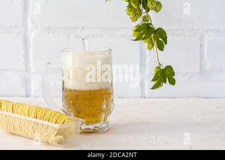 Glas Becher Bier mit Kartoffelchips und einem Hopfenzweig auf weißem Hintergrund. Stockfoto