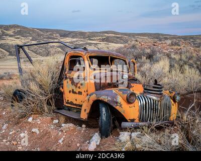 Alte rostigen Abschleppwagen an Colorado Ausläufern von Büschen überwuchert. Herbstlandschaft in der Dämmerung Stockfoto