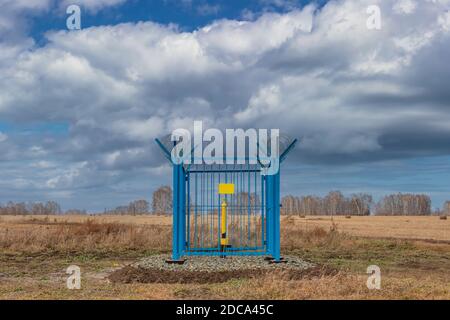 Aufnahme einer eingesperrten Industriegasstation mit Stacheldraht auf dem Zaun. Gelbe Gasleitung in der Mitte des Käfigs, leere gelbe Platte am Zaun. Stockfoto