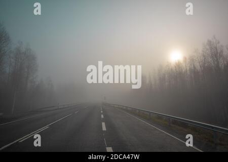 Schlechte Sicht. Die Straße ist in starkem Nebel, entlang der Ränder der Straße gibt es einen Wald. Herbstmorgen im November. Foto durch die Windschutzscheibe eines Autos. Hochwertige Fotos Stockfoto