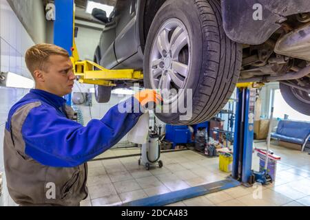 Nahaufnahme eines Mechanikers, der die Oberfläche eines Autoreifens mit einer Sprühflasche sehr aufmerksam überprüft. Mechaniker mit blauem Overall und orangefarbenen Handschuhen. Auto Stockfoto