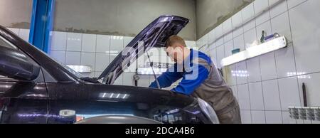 Ein Automechaniker unter der Haube, Arbeiten an einem Automotor. Mechaniker sieht sehr ernst und konzentriert. Stockfoto