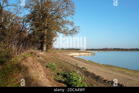 Ein See, der durch eine Sandgrube geschaffen wurde. Einige Laubbäume und Sträucher. Schöner sonniger Morgen mit klarem blauen Himmel im Herbst. Stockfoto