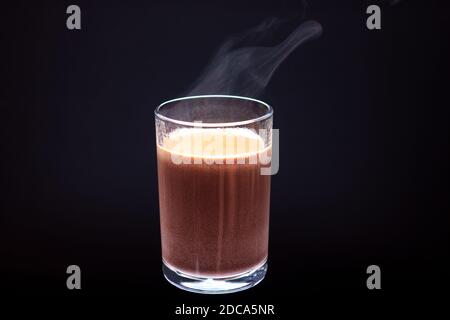 Glas mit Heißgetränk und Dampf auf schwarzem Hintergrund. Stockfoto