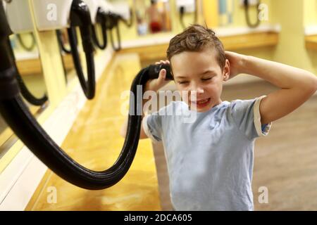 Das Kind trocknet die Haare mit dem Haartrockner in der Umkleidekabine des Fitnessraums Stockfoto