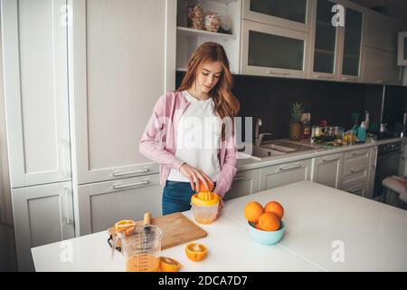 Kaukasische Ingwer Frau mit Sommersprossen wird manuell gepresst Orangensaft In der Küche Stockfoto