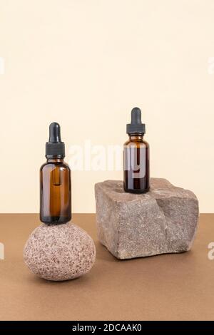 Zwei kosmetische braune Glasflaschen mit Pipette auf Steinen, beigefarbener brauner Hintergrund. Natürliches organisches Spa Kosmetikkonzept. Vorderansicht Kopierbereich Stockfoto