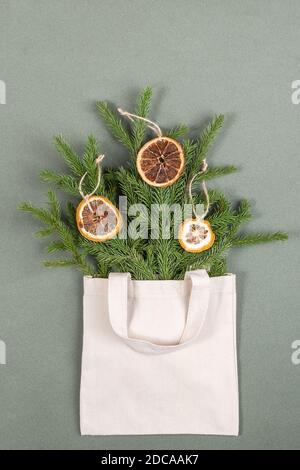Ein Bouquet von Tannenzweigen mit Kreisen getrockneter Orangen in Stoff Öko-Tasche auf grünem Hintergrund. Konzept umweltfreundlich und ohne Verschwendung. Draufsicht Flat Lay. Stockfoto