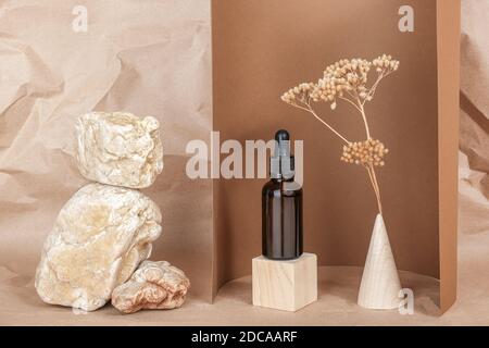 Serum, ätherische Öle oder flüssiges Kollagen in brauner Glasflasche mit Pipette auf geometrischen Holzformen, snone und getrocknete Blüten auf beige, braunes Backgr Stockfoto