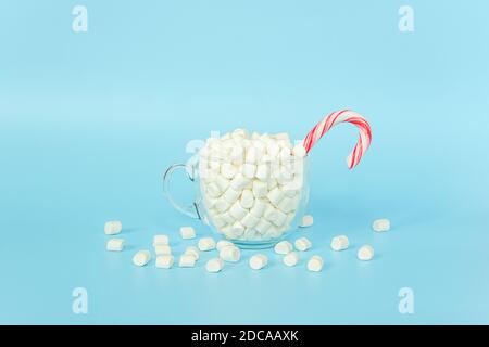 Große transparente Tasse Marshmallows mit rotem Lollipop Stock auf blauem Hintergrund. Frohe Weihnachten oder Happy New Year Konzept. Minimaler Stil, Draufsicht, FLA Stockfoto