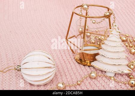 Dekorativer weihnachtsbaum, goldener Kerzenständer, Kugel und goldene Girlande auf rosa gestricktem Hintergrund. Neujahrs- oder Weihnachtskonzept. Vorlage für Design, Stockfoto