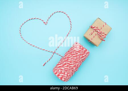 Weihnachtsdekoration rot-weiß Garn in Form von Herz und Geschenkbox auf blauem Hintergrund. Konzept weihnachten Geschenkverpackung . Draufsicht Flat Lay Copy s Stockfoto