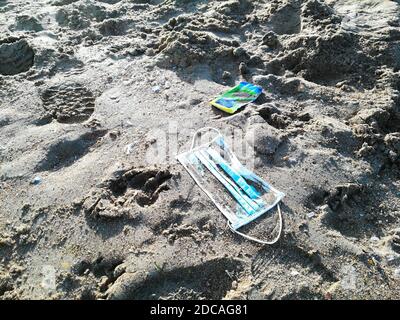 Eine blaue Mundmaske auf den Sand des Strandes geworfen Mit dem farbigen Plastikbeutel von Taschentüchern im harten Herbst Leichte und menschliche Fußabdruck Stockfoto