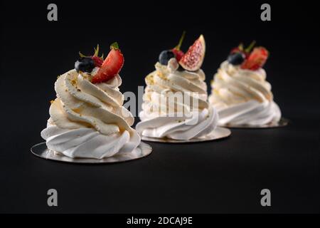 Drei Mascarpone Desserts in Reihe mit Feigenscheiben, Erdbeere, Heidelbeere und Himbeere dekoriert. Frische leckere Schlagsahne mit Beeren isoliert auf schwarzem Hintergrund. Stockfoto