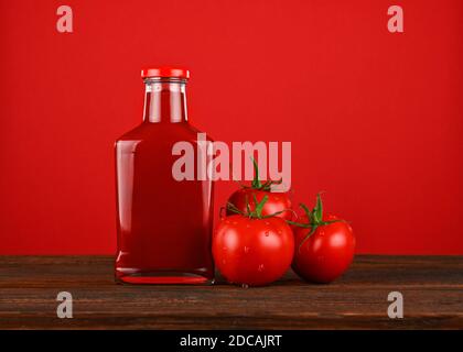 Nahaufnahme eine Glasflasche Ketchup-Sauce und frische Tomaten auf Holztisch auf rotem Hintergrund mit Kopierraum, Low-Angle-Ansicht Stockfoto