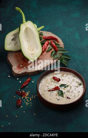 Frische grüne Papaya, aufgeteilt in zwei Stücke und angeordnet auf Ein Holzstück mit trockener roter Chili und Curryblättern Daneben und eine Holzschüssel voll mit r Stockfoto