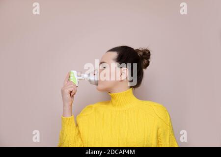 Eine 40-jährige Frau in einem gelben Pullover auf rosa Hintergrund inhaliert die oberen Atemwege, die Lunge mit Hilfe eines kabellosen Verneblers. Augen Stockfoto