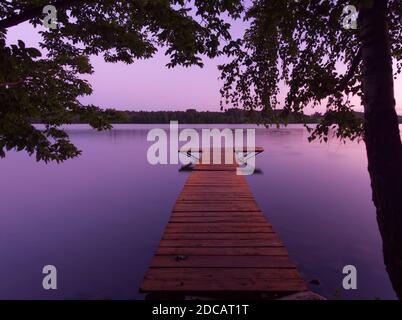 Hölzerner Steg auf dem stillen Wasser des Sees Rospuda Filipowska bei Sonnenuntergang. Stockfoto
