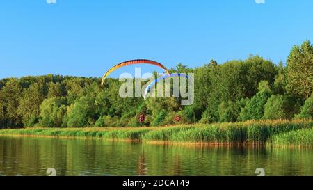 Zwei motorbetriebene Hängegleiter fliegen mit den grünen Bäumen und einem blauen Himmel im Hintergrund. Stockfoto