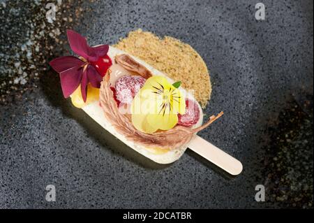 Eis mit Blumen und Früchten auf schwarzem Teller Makro Anzeigen Stockfoto