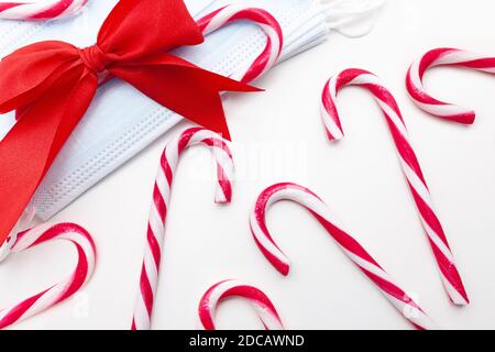 Blaue medizinische Gesichtsmasken mit roter Schleife und roten und weißen Süßigkeiten Stöcke, Weihnachtskonzept Stockfoto