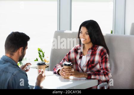 Happy african american Frau hält Einweg-Tasse in der Nähe Mann mit Händedesinfektionsmittel auf verschwommenem Vordergrund Stockfoto