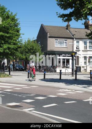 London, Großbritannien. Ein Radfahrer nähert sich einer Kreuzung auf der Ruckholt Road. Teil des Mini-Holland-Programms von Waltham Forest für sicherere Straßen. Fahrradladen im Hintergrund. Stockfoto